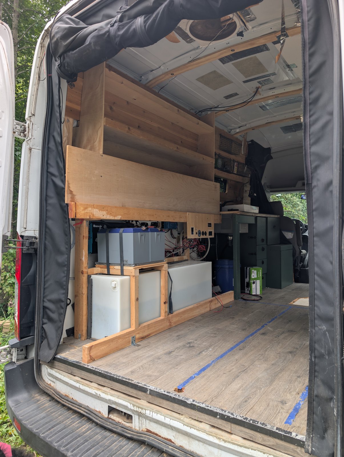Interior from the rear doors, with the battery, water tank, electrical panel and shelving along the wall