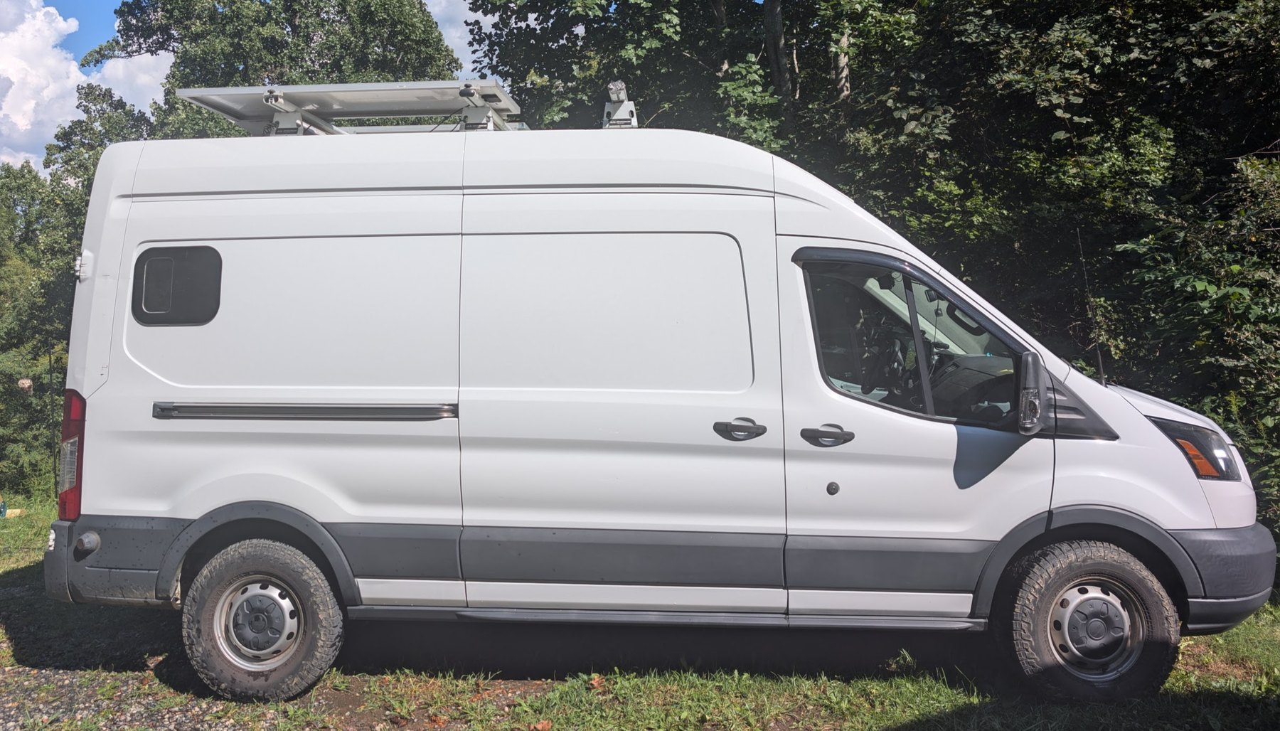 Passenger side profile of the high-roof Transit, showing the added window, roof rack and all-terrain tires