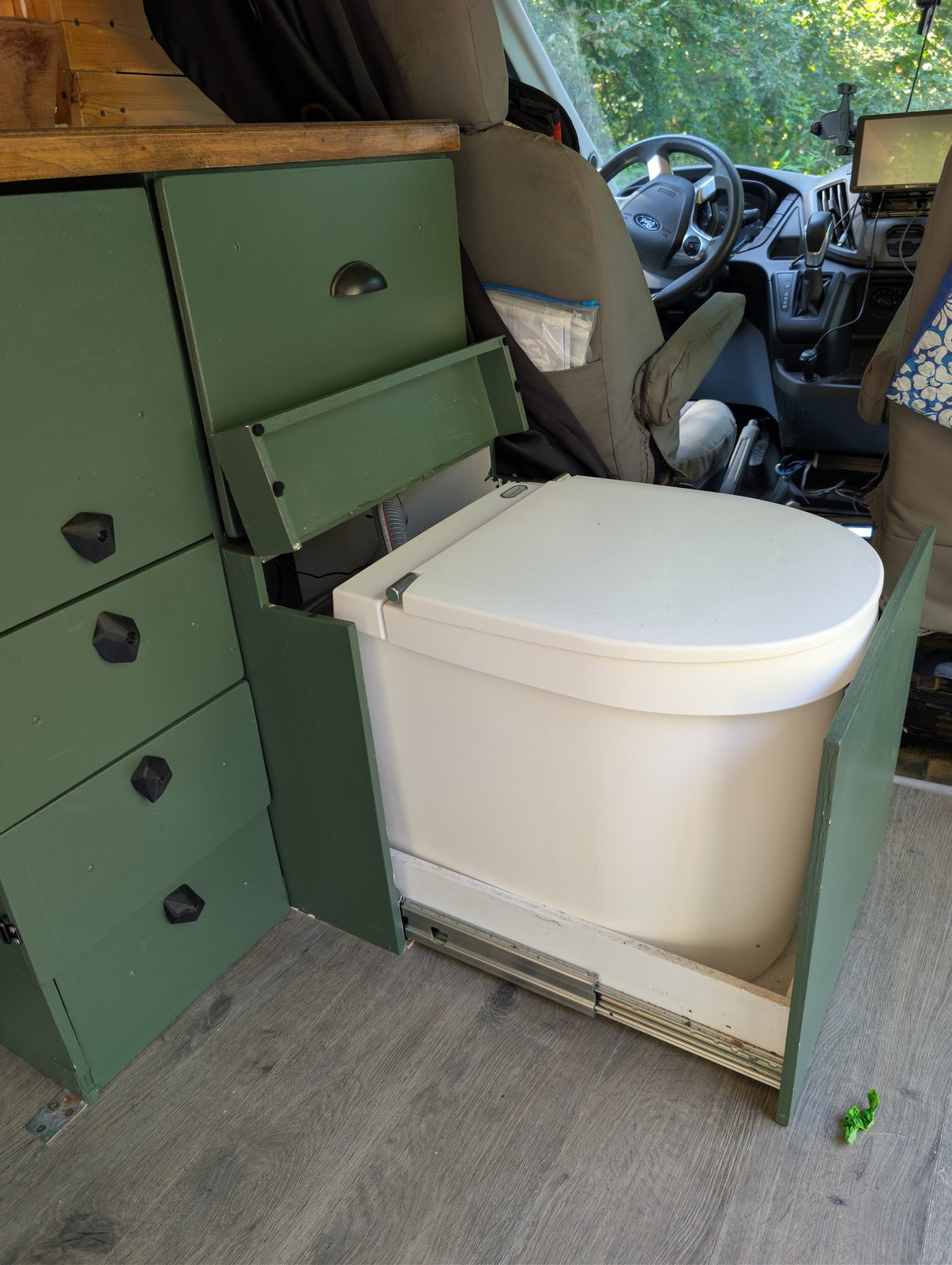 The Separett toilet on a slide-out drawer inside the green cabinetry, with the cab beyond